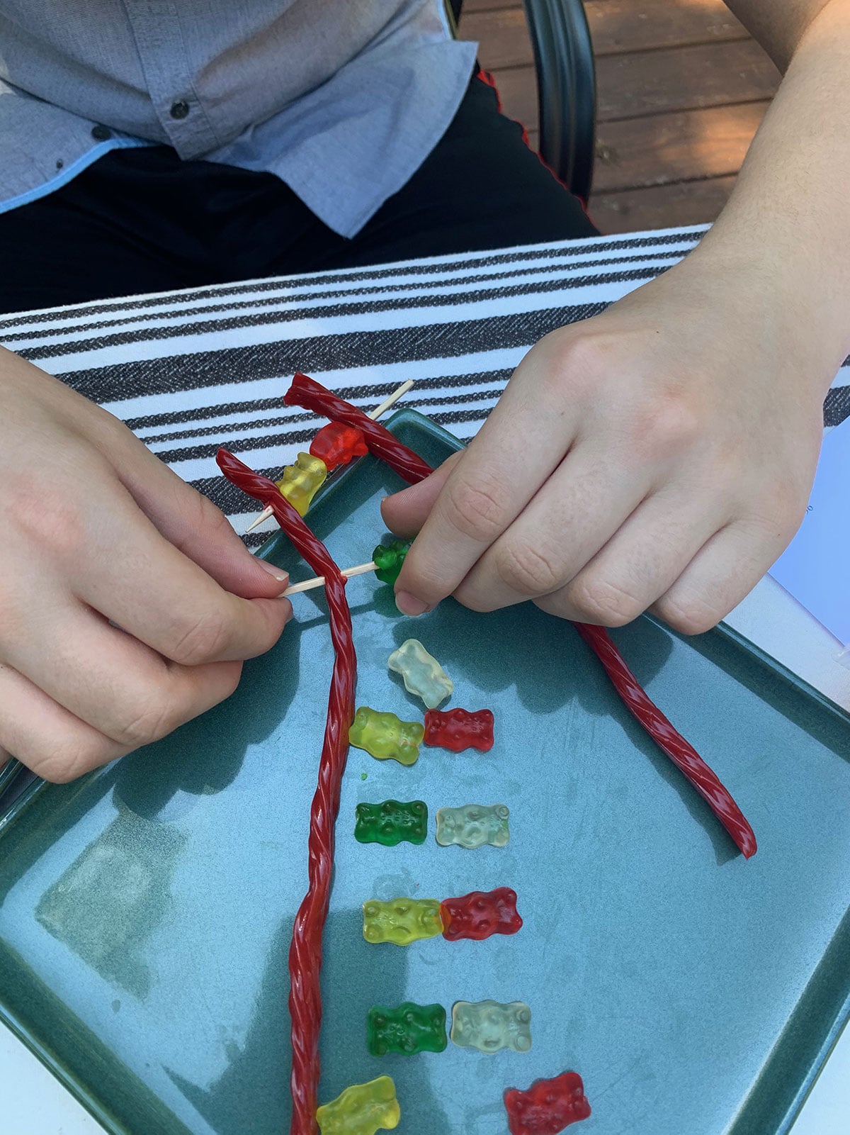 A young man aligns two twizzlers in parallel and prepares to stick gummy bears on toothpicks